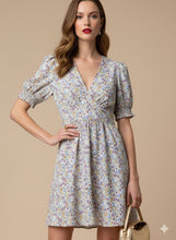 Cargar imagen en el visor de la galería, Vestido Lucía - Este encantador vestido corto, confeccionado en una tela ligera y fluida con una caída impecable, destaca por su delicado estampado floral en tonos lila, azul y ocre sobre un fondo neutro.